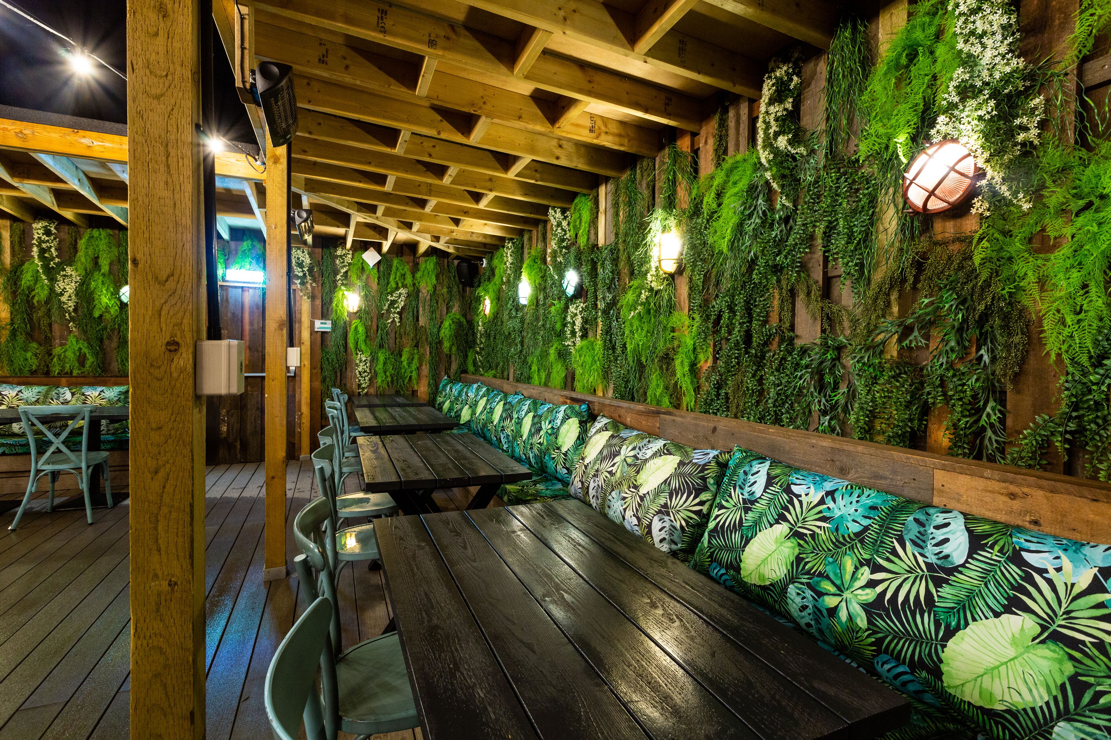 An indoor dining area with wooden tables and benches, surrounded by walls covered in green foliage.