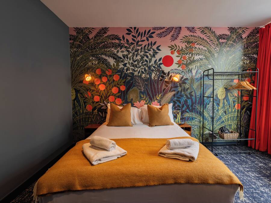 A hotel room with a bed, a mural on the wall, and a red curtain.