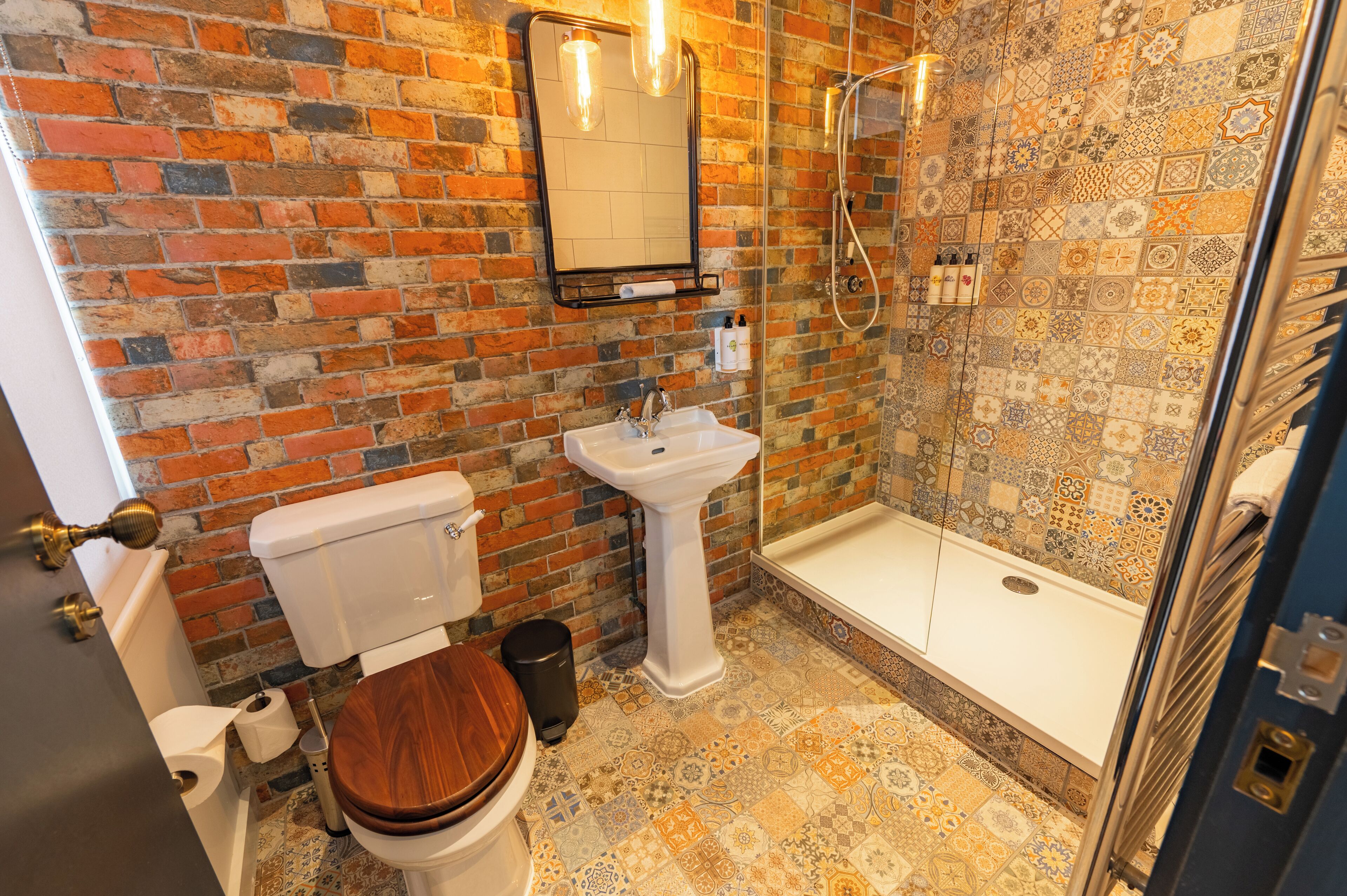 A bathroom with a brick wall, a toilet, a sink, and a shower.