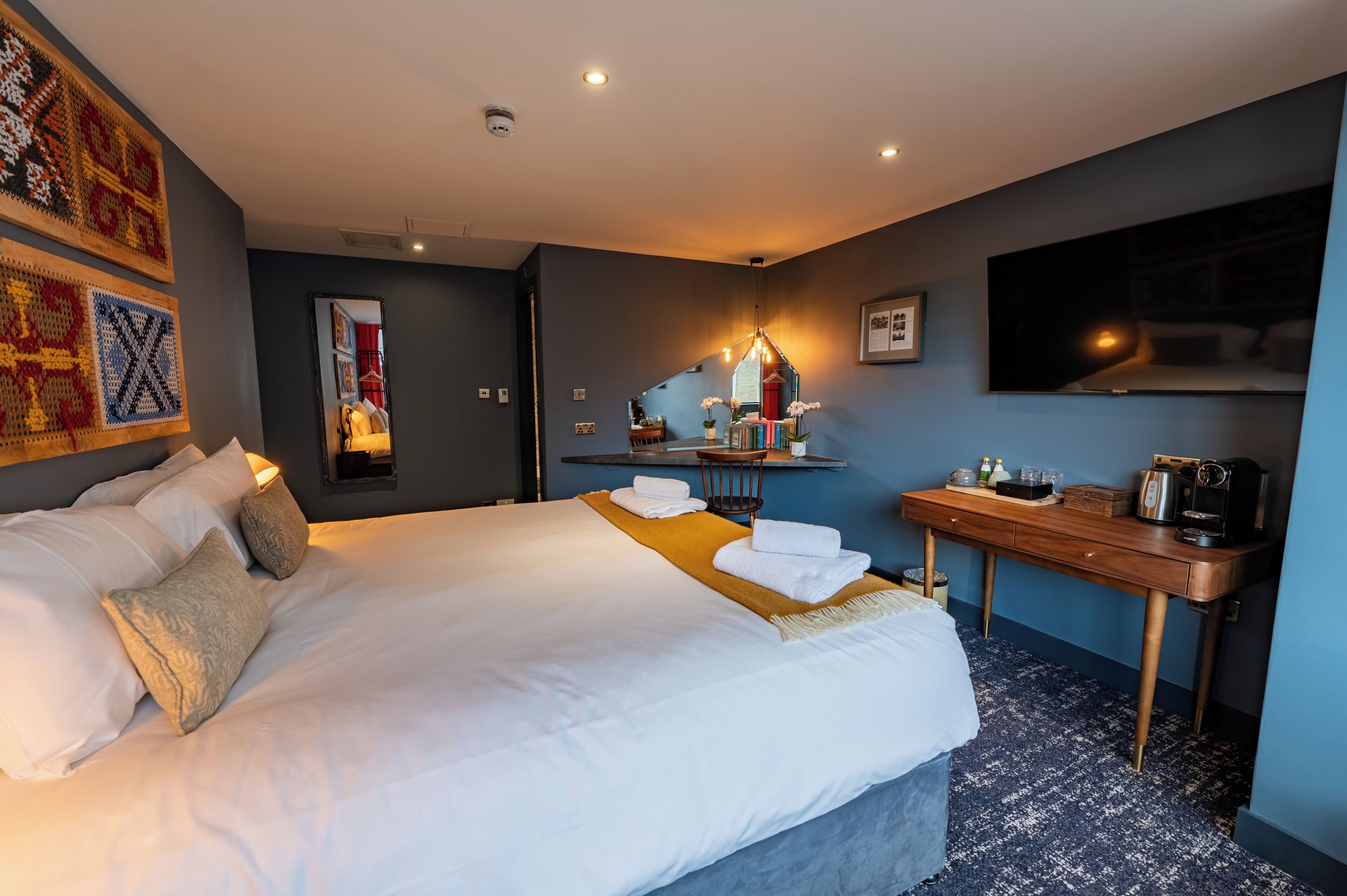 A hotel room with a large bed, a wooden desk, a mirror, and a television.