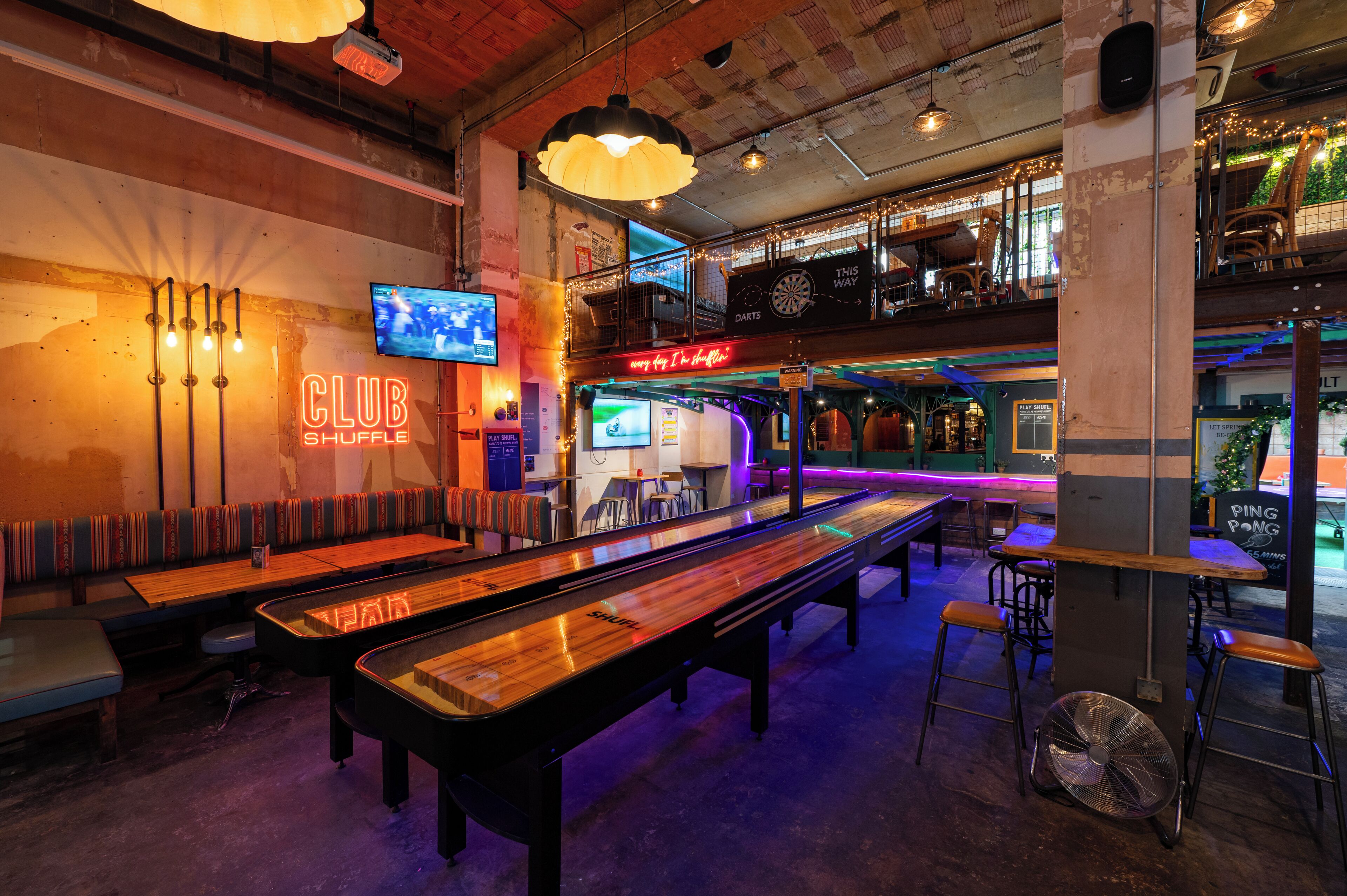 A billiards hall with multiple tables, a neon sign, and a television screen.