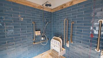 Un baño con paredes de azulejos azules, suelo de madera, ducha con cabezal de ducha de mano y un inodoro blanco.