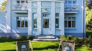 A two-story building with a balcony on the second floor, a front door, and two lawn chairs in front. - Villa Testa (Sopot)