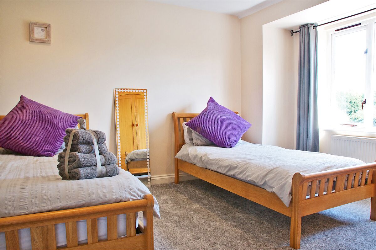 A bedroom with two wooden beds, each with a purple pillow and a rolled towel. A full-length mirror is on the wall between the beds.