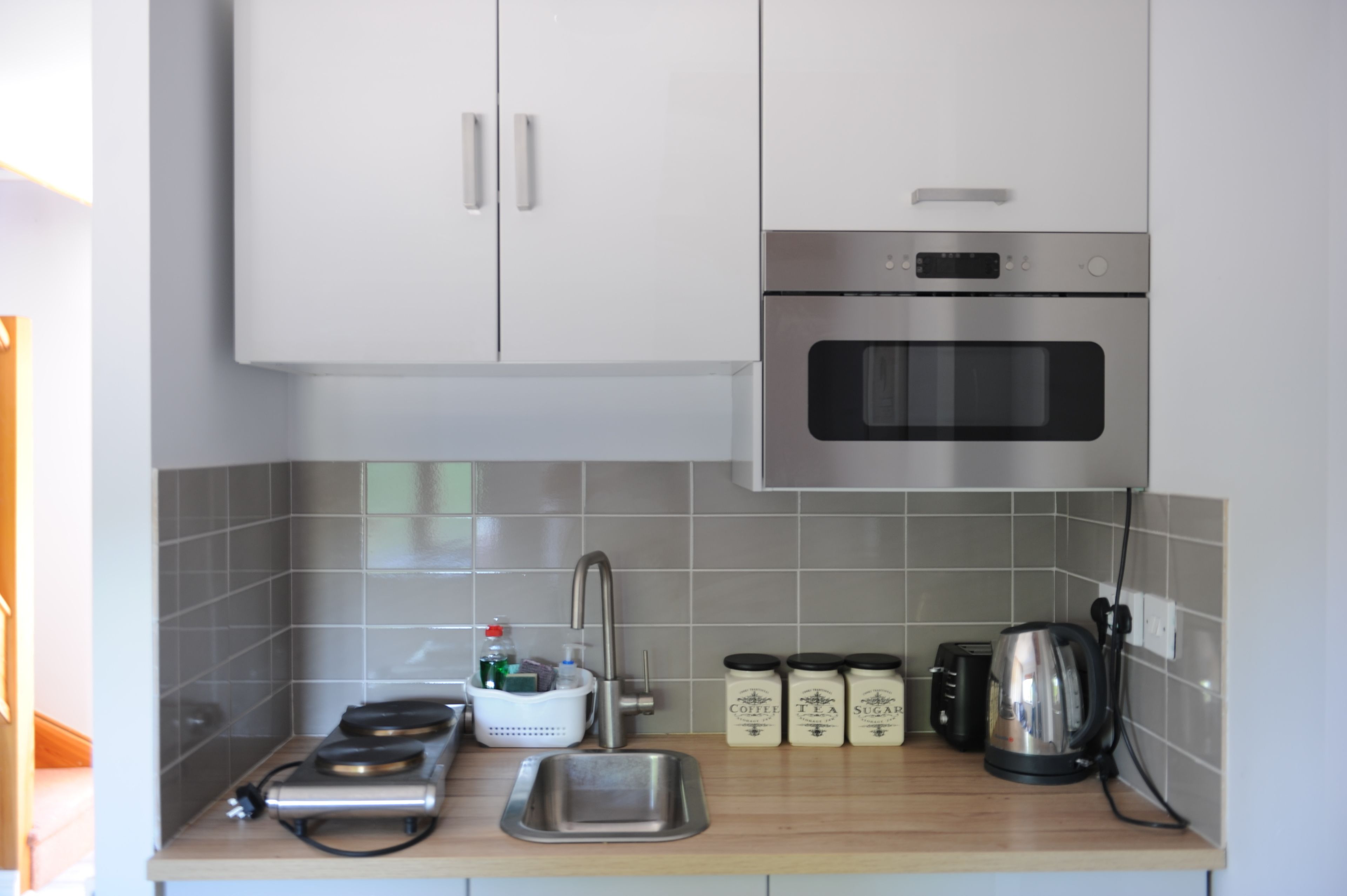 A kitchen with white cabinets, a stainless steel oven, a sink, and a kettle.