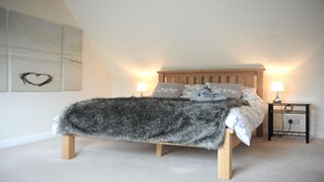 Een slaapkamer met een houten bed, twee bedlampen, een hartvormige decoratie aan de muur en een zachte plaid.