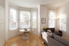 A bright living room with a round table, a sofa, and large windows with blinds. - Fox Den (Nottingham)