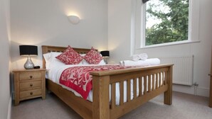 Un dormitorio con una cama de madera, dos mesitas de noche, una lámpara y una ventana con vistas a árboles.