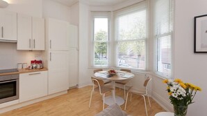 Una cocina moderna con armarios blancos, una mesa de comedor con sillas y un ventanal con persianas.