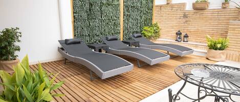Een zonnig terras met een loungegedeelte, met drie comfortabele stoelen, een ronde metalen tafel en een houten dek.