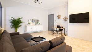 Uma sala de estar moderna com sofá seccional, uma mesinha de centro, uma área de jantar com mesa e cadeiras, uma TV fixada na parede e um vaso de planta.