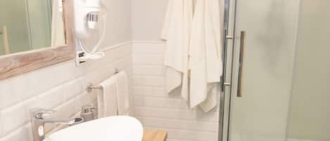 A modern bathroom with a wooden vanity, a white sink, a glass shower enclosure, and two white towels hanging on the wall.