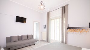 Quarto com cama, sofá, televisão e janela com cortinas.
