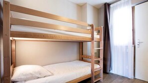 Cama litera con estructura de madera, colchón blanco y almohada. Se observa una puerta con cortina a la derecha.