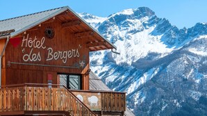 Un edificio de madera con un balcón y un paisaje montañoso, identificado con el letrero "Hotel des Bergers".