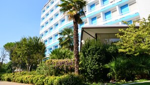 Een meerlaags hotel met een blauw-witte gevel, omringd door weelderige begroeiing en palmbomen.