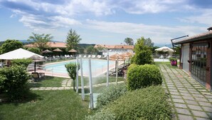 A pool area with lounge chairs and umbrellas, surrounded by greenery and a brick building. - La Locanda di Corrado (Cerreto Guidi)