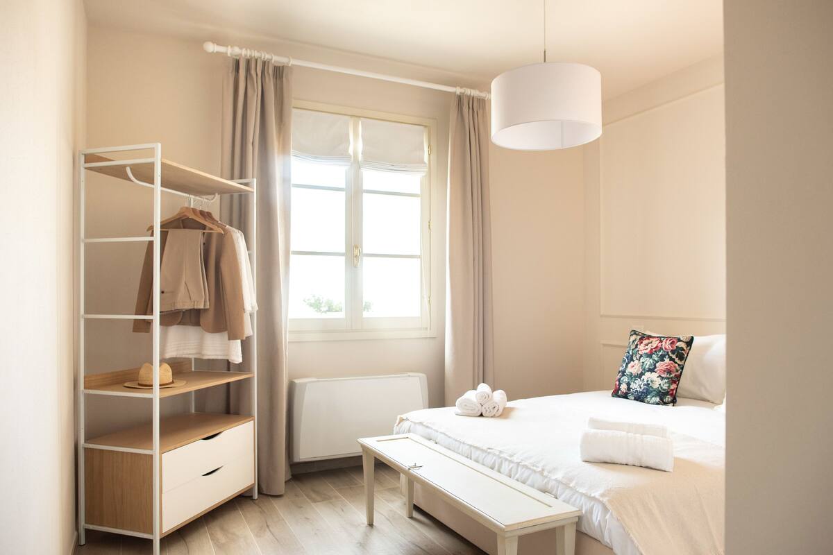 Een slaapkamer met een bed, nachtkastje, kledingrek en een raam met gordijnen.