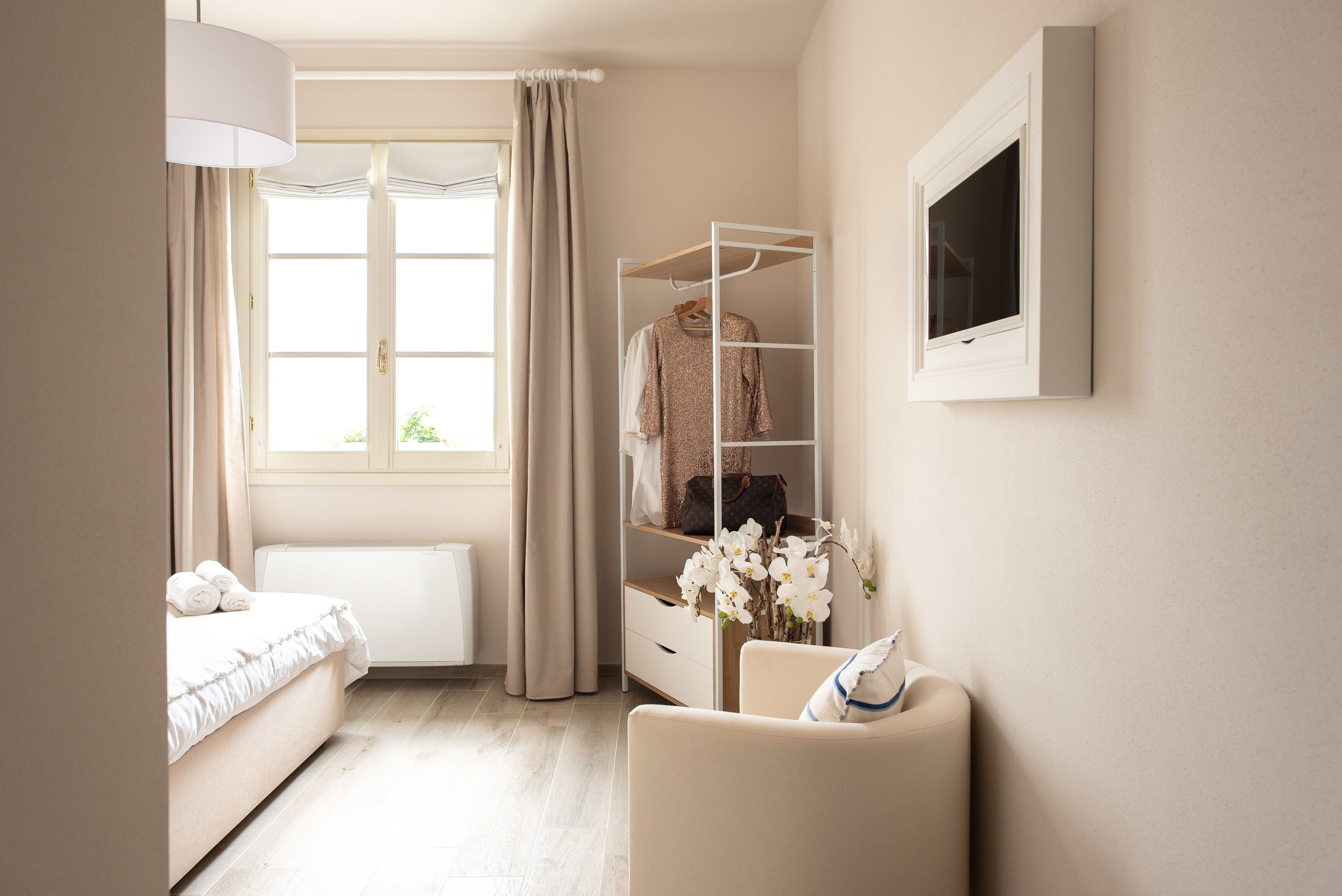 A bedroom with a bed, a bedside table, a chair, a wardrobe, and a window with curtains.