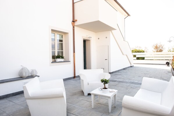 A modern outdoor patio with white furniture, a potted plant, and a white wall with a window and door. - La Locanda di Corrado (Cerreto Guidi)