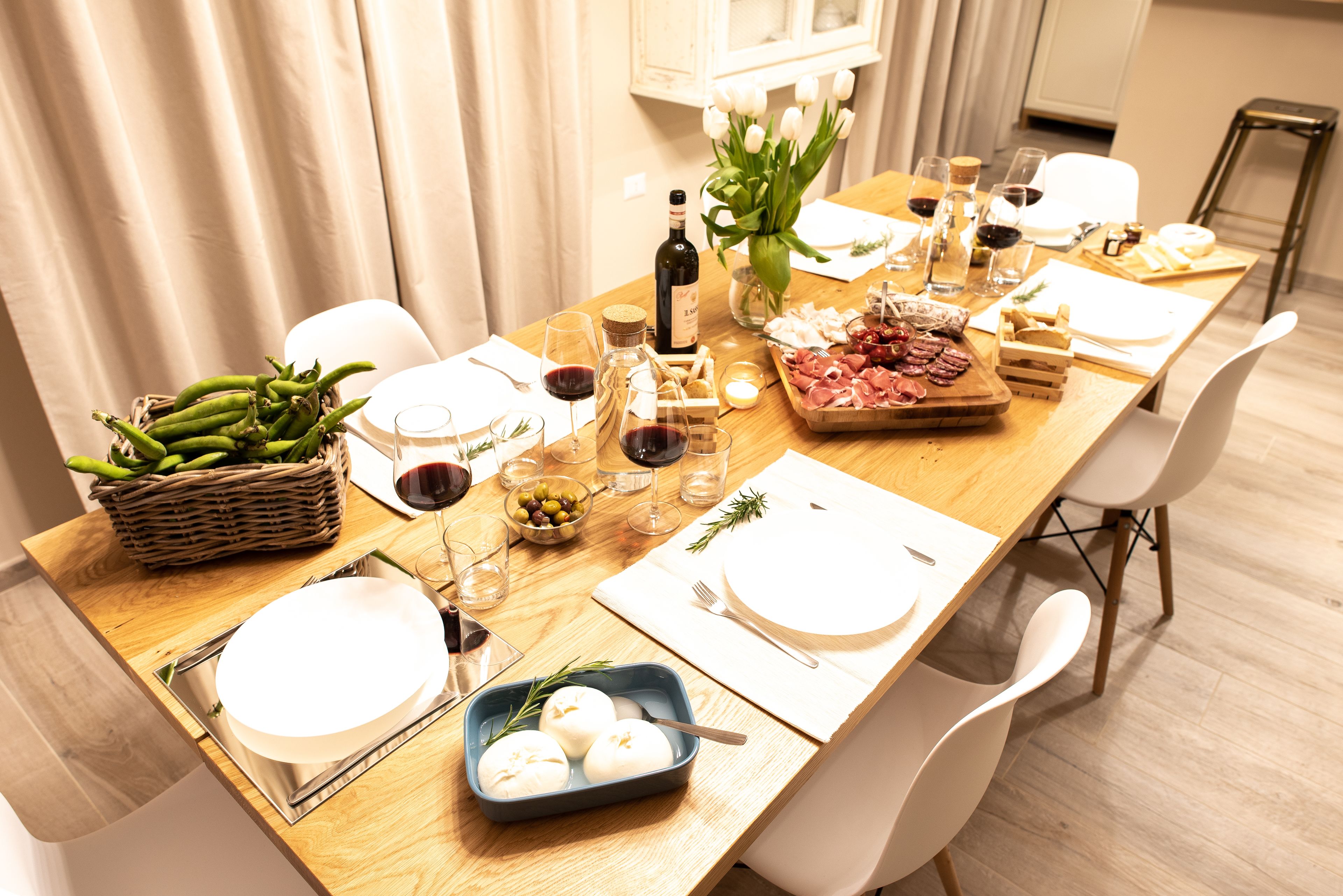 A dining table set with plates, glasses, a bottle of wine, and a variety of food items.
