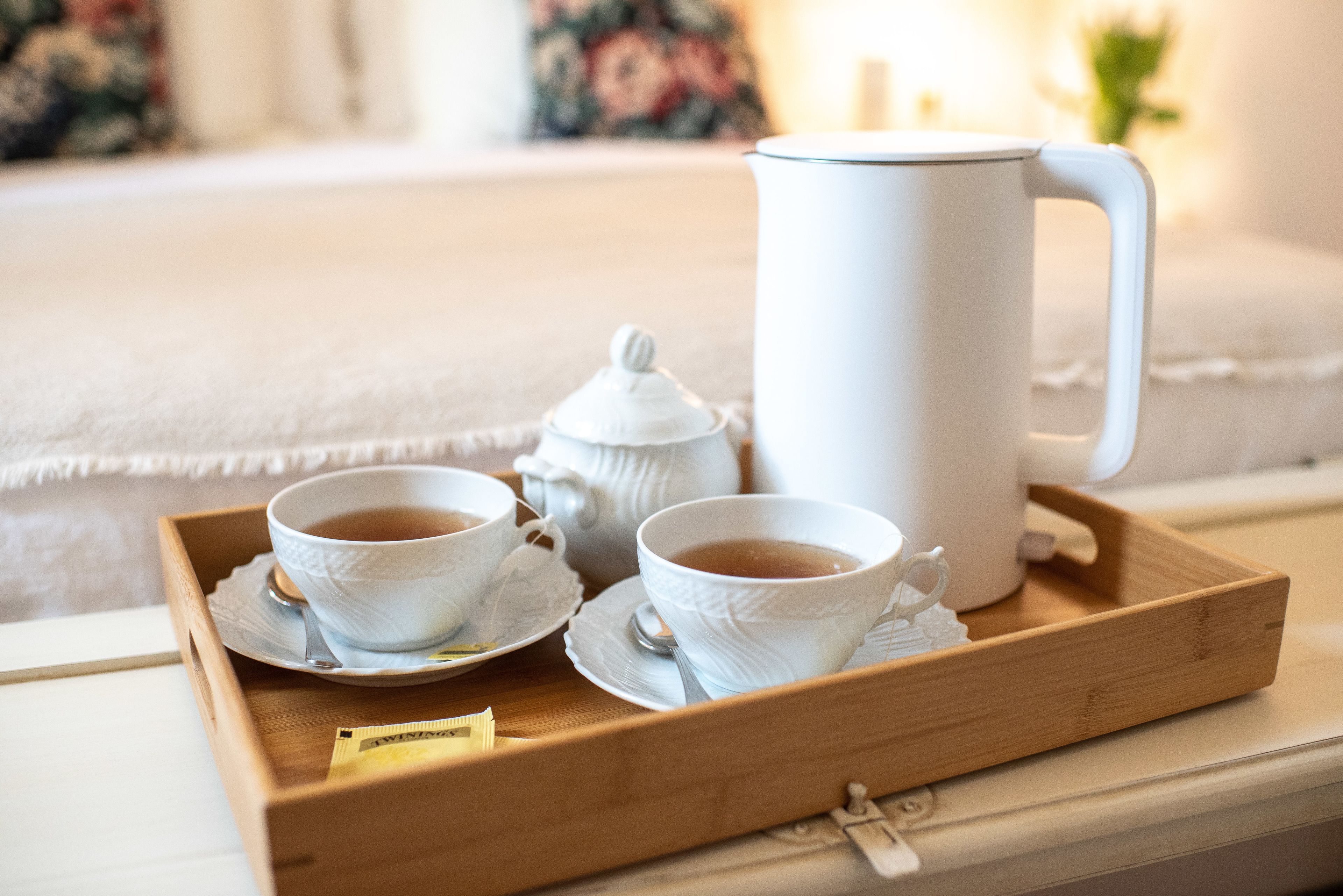 A tray with two white cups of tea, a white teapot, and a white mug on a wooden tray.