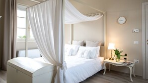 A four-poster bed with white linens, a bedside table with a lamp, and a clock on the wall. - La Locanda di Corrado (Cerreto Guidi)