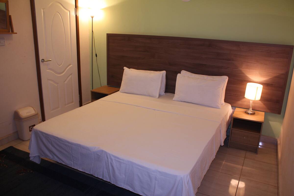 A neatly made bed with white linens, a wooden headboard, and a bedside lamp.