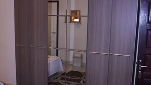 Una habitación con armario, cama con colcha blanca y alfombra estampada.