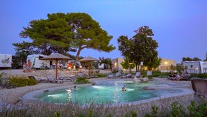 A pool area with lounge chairs and umbrellas, surrounded by trees and buildings. - Mobile Homes at Camping Ugljan Resort (Preko)