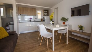 A modern kitchen with white cabinets, a dining table with chairs, and a TV mounted on the wall. - Mobile Homes at Camping Ugljan Resort (Preko)