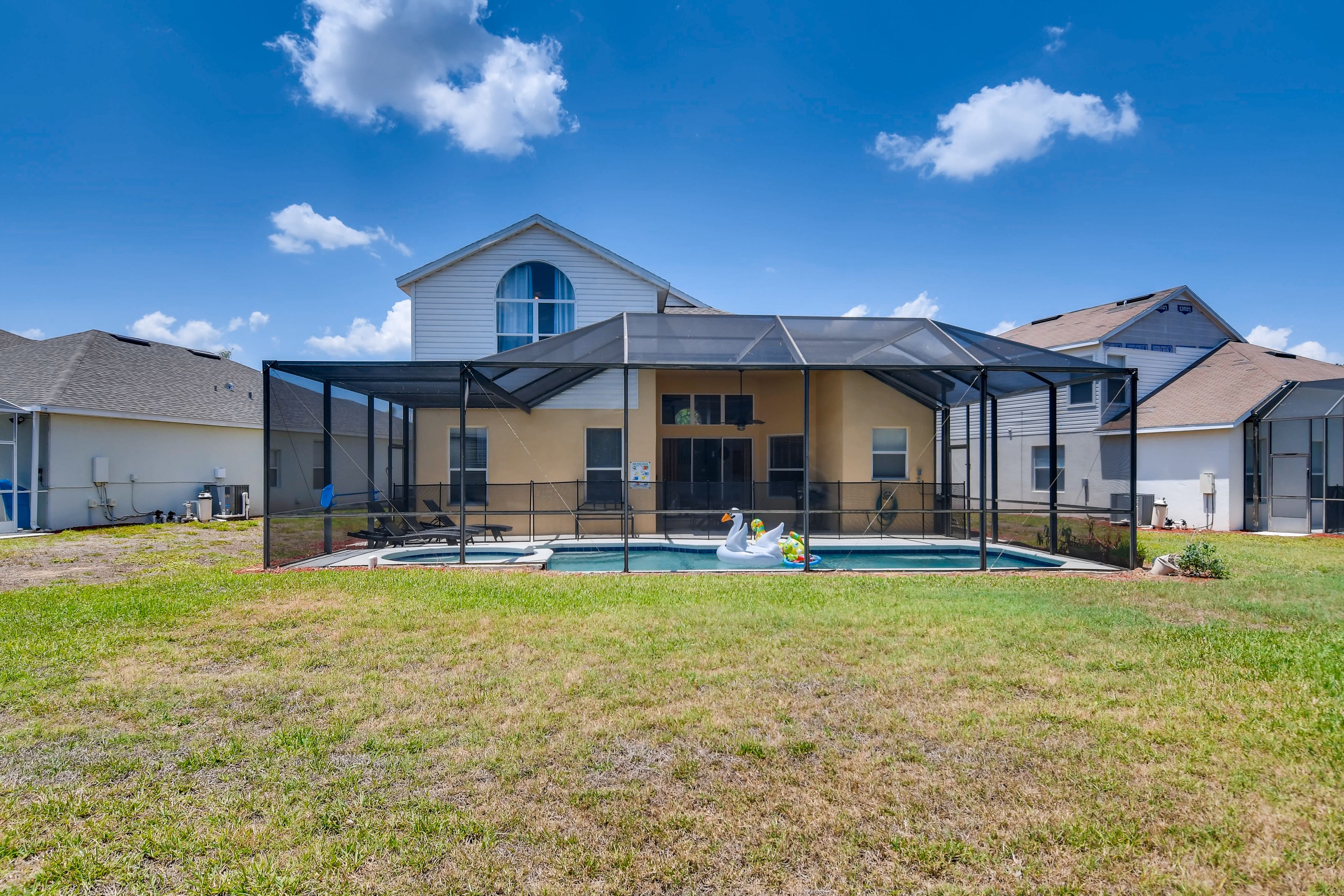A residential property with a covered patio, a swimming pool, and a swan inflatable decoration.