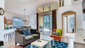 Ein modernes Wohnzimmer mit Sofa, Couchtisch und einem Essbereich mit Küche im Hintergrund.
