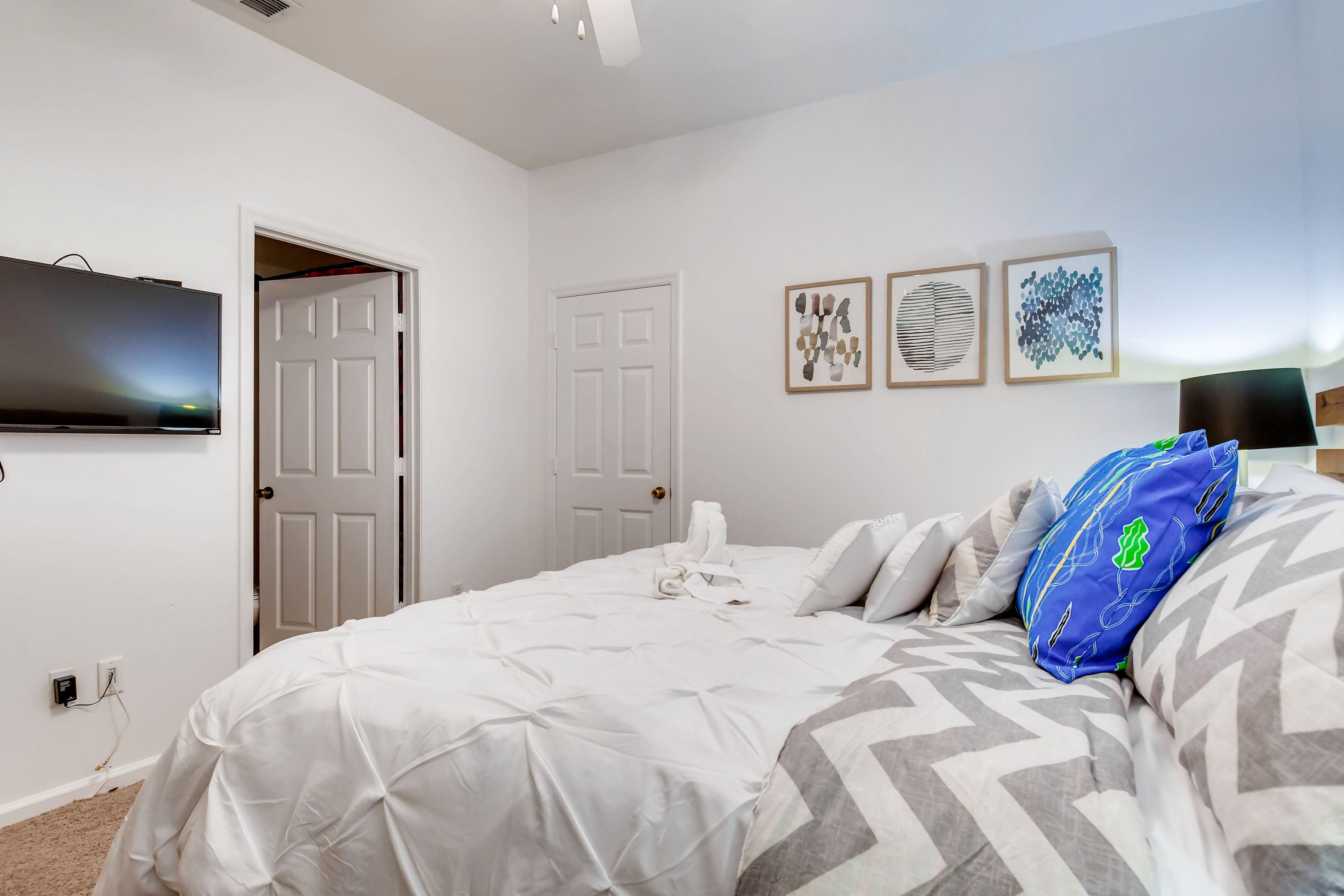 A bedroom with a bed, a TV mounted on the wall, and a door leading to another room.