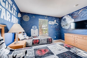 A Star Wars-themed bedroom with a galaxy wall mural, a bed with Star Wars bedding, a wooden dresser, and a Star Wars poster on the wall.