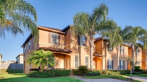 A two-story residential building with a brick facade, multiple windows with shutters, and a well-maintained lawn with palm trees. - 4BR Home in Regal Palms by FS FL VH-844 (Davenport)