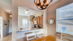 A modern kitchen with wooden cabinets, a granite countertop, and a dining area with a wooden table and white chairs. - 4BR Home in Regal Palms by FS FL VH-844 (Davenport)