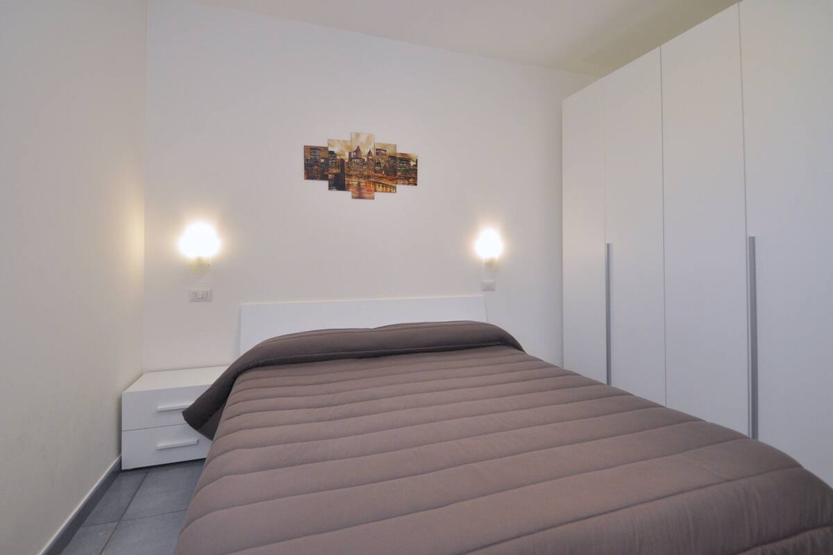 A bedroom with a bed, a nightstand, a wall-mounted light, and a wardrobe.