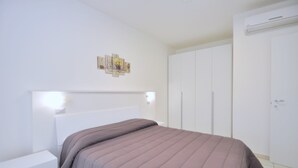 Une chambre à coucher comprenant un lit, des tables de chevet, une armoire et un luminaire fixé au mur.