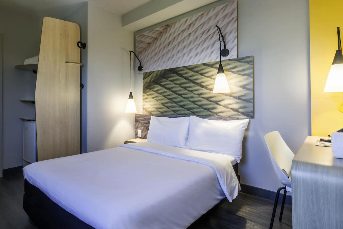A hotel room with a bed, bedside tables, a desk, a chair, and a wardrobe.