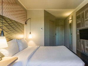 Una habitación de hotel con cama, lámpara de noche, teléfono y televisor montado en la pared.