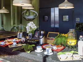 A breakfast setup with coffee machines, a coffee grinder, and a variety of breakfast items on trays.