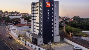 Un moderno edificio de hotel con un llamativo logotipo de 'ibis', varios pisos y un área de estacionamiento.
