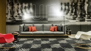 Un área de descanso moderna con un sofá gris, cojines rojo y negro, un tapete con estampado en blanco y negro, y una mecedora roja.