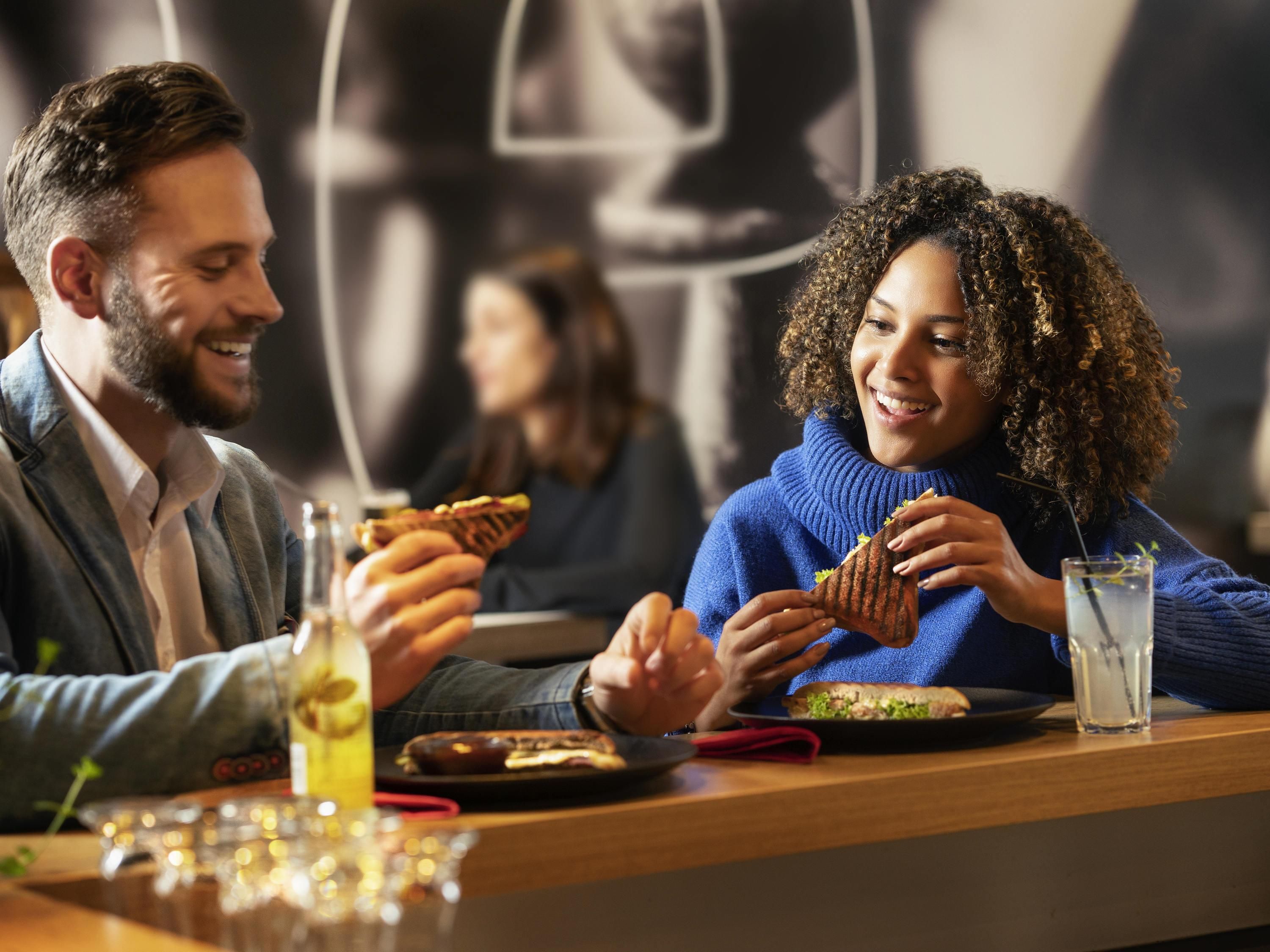 Zwei Personen essen in einem Restaurant an einem Tisch, mit einem Getränk und einem Teller Essen.