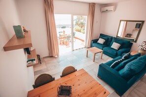 A modern living room with a wooden table, teal sofas, and a sliding glass door leading to an outdoor area. - APARTAMENTOS PUERTO MARINA DEL ESTE (Almunecar)