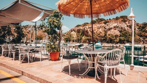 Outdoor seating with umbrellas, a potted plant, and a view of boats and hills. - APARTAMENTOS PUERTO MARINA DEL ESTE (Almunecar)