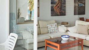A modern living room with a glass door leading to a balcony, a beige sofa, a wooden coffee table, and two wall-mounted paintings. - APARTAMENTOS PUERTO MARINA DEL ESTE (Almunecar)