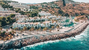A coastal town with a marina, white buildings with red roofs, and a rocky shoreline. - APARTAMENTOS PUERTO MARINA DEL ESTE (Almunecar)