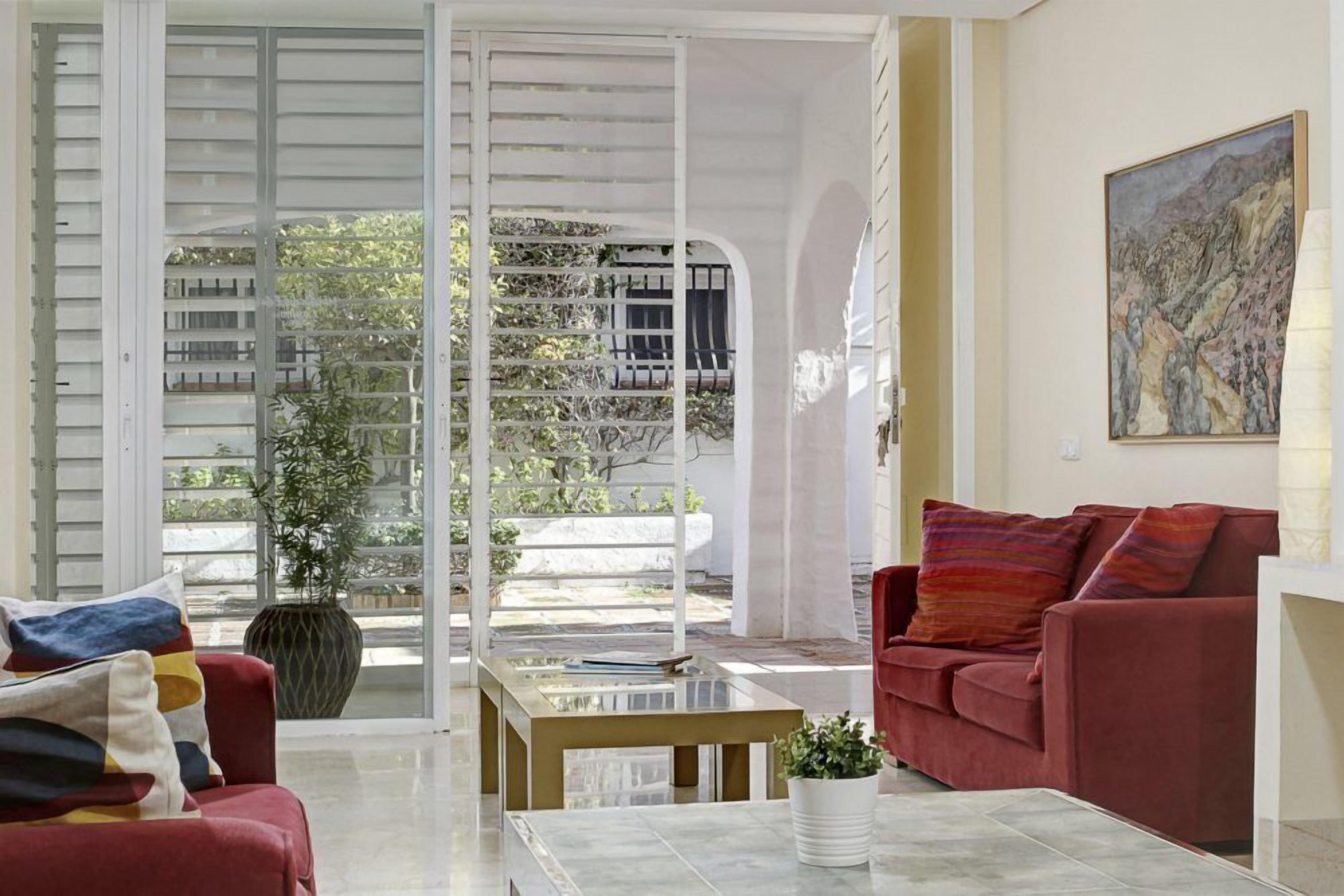 A modern living room with a red sofa, a glass coffee table, and a large window with a view of a balcony.